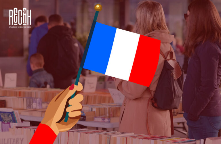 Visiteurs dans un salon du livre avec un drapeau français au premier plan.